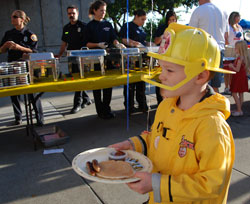 Child in firefighter costume carrying plate with pancake