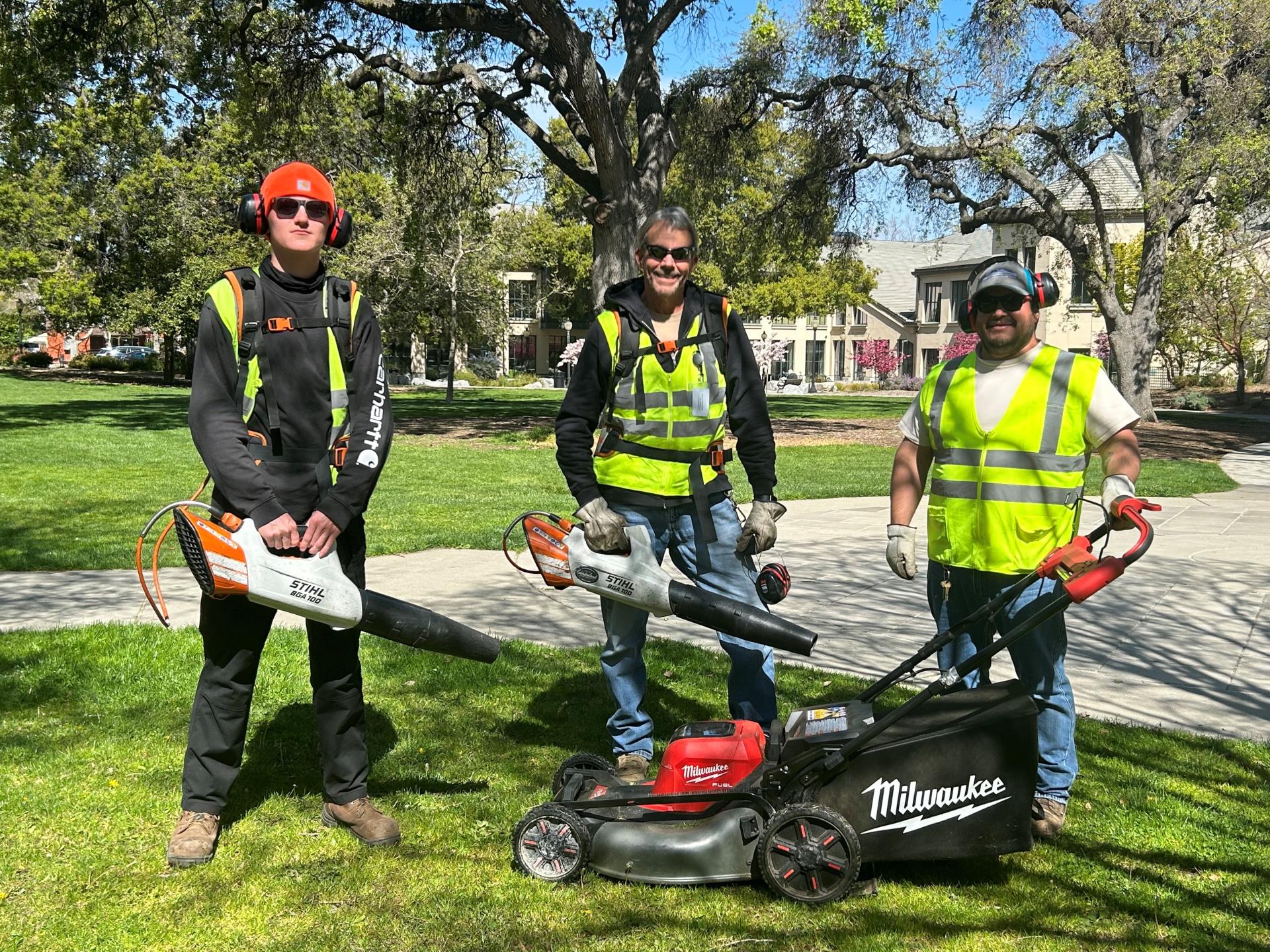 Workers pose in park with electric yard equipment